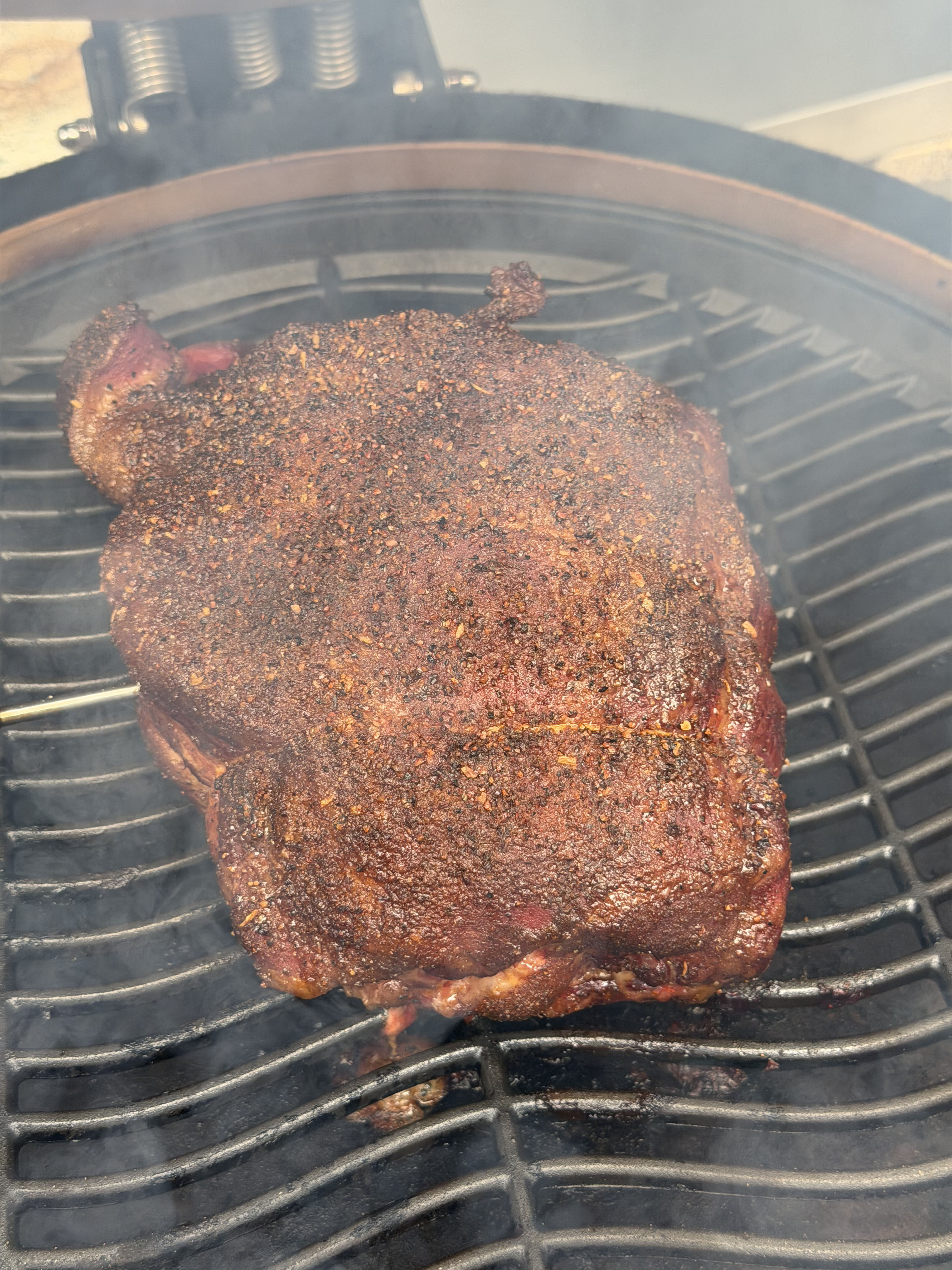A smoked brisket resting on a cutting board beside a pellet grill
