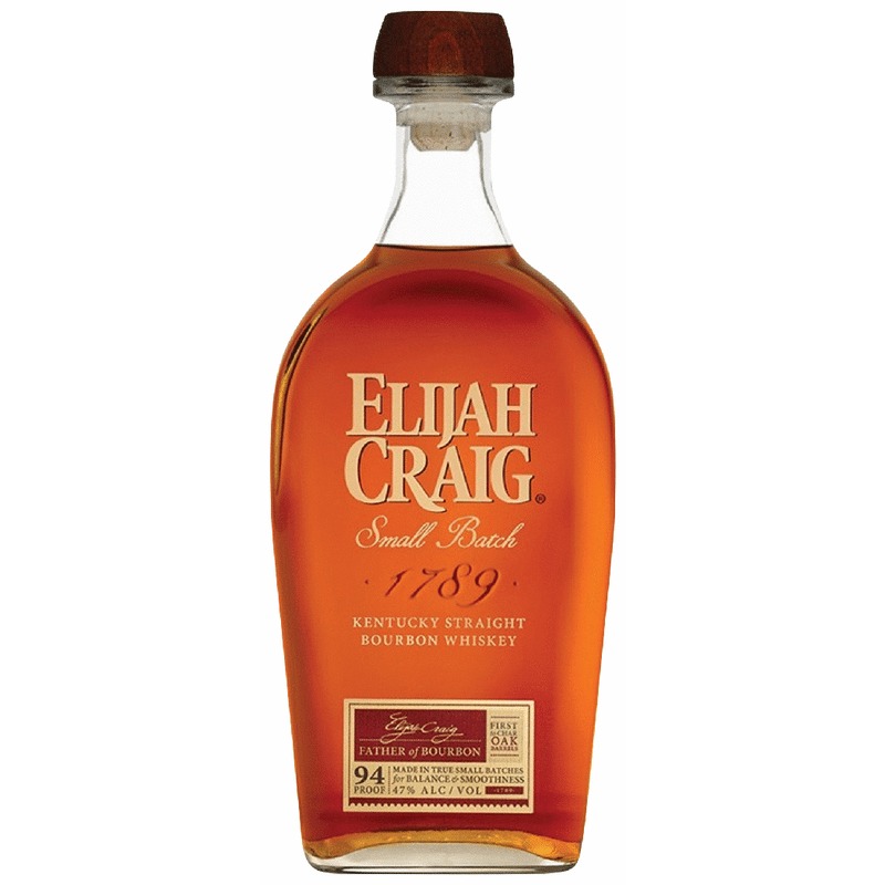 A glass of bourbon beside a candle on a dark bar